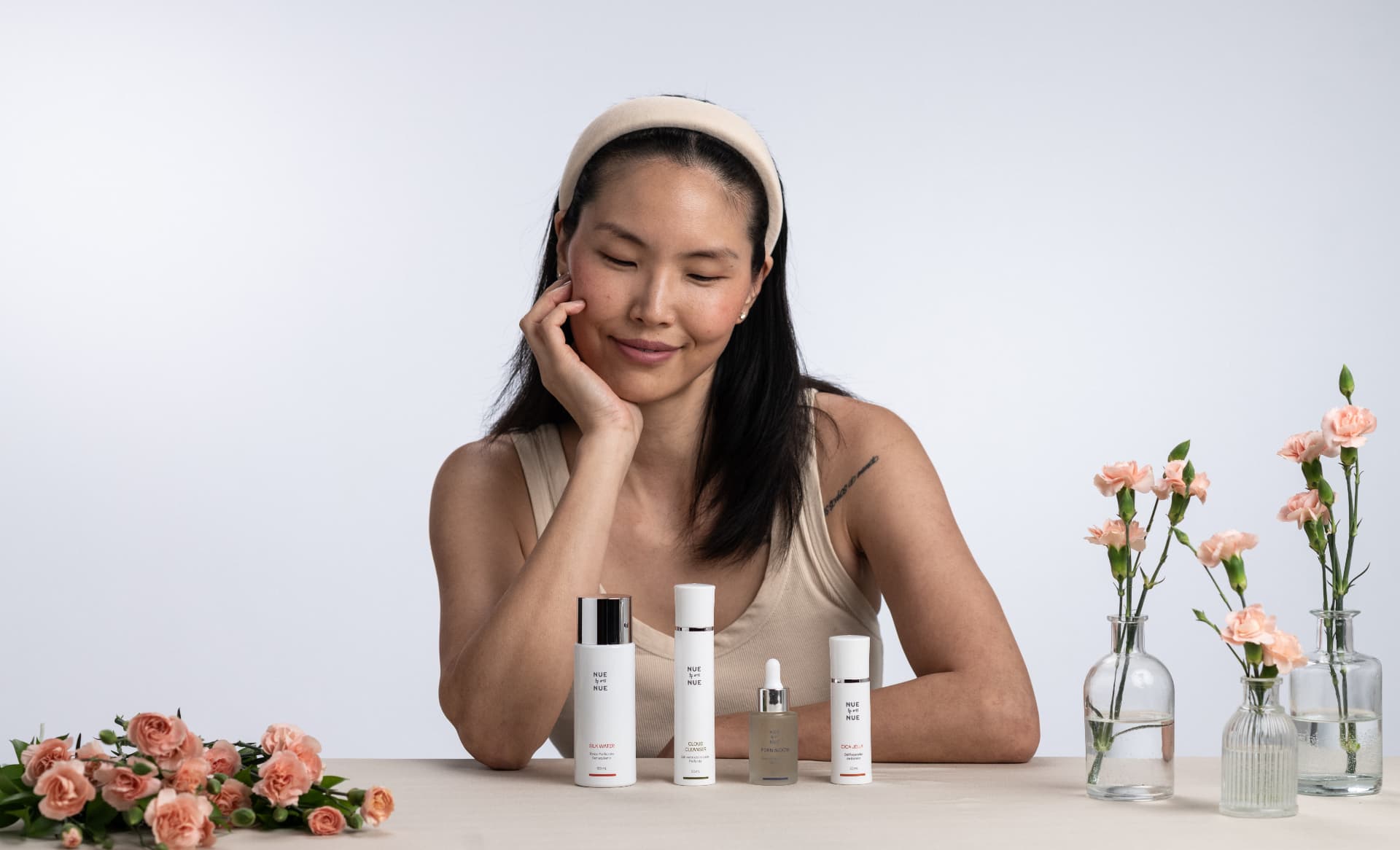 Mulher olhando para a linha de skincare Nue Nue, com flores rosadas